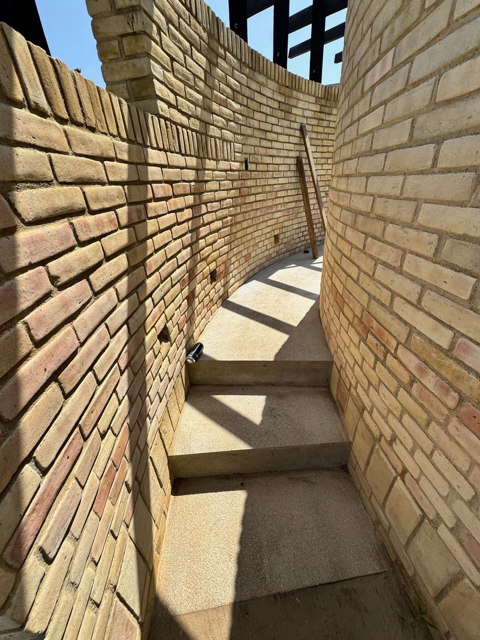 Las paredes de ladrillo se curvan alrededor de escaleras estrechas con luz solar brillante.
