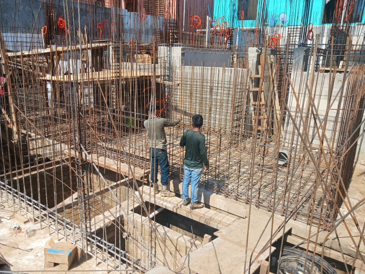 Dos trabajadores de la construcción de pie entre estructuras de barras de acero en un sitio de construcción.