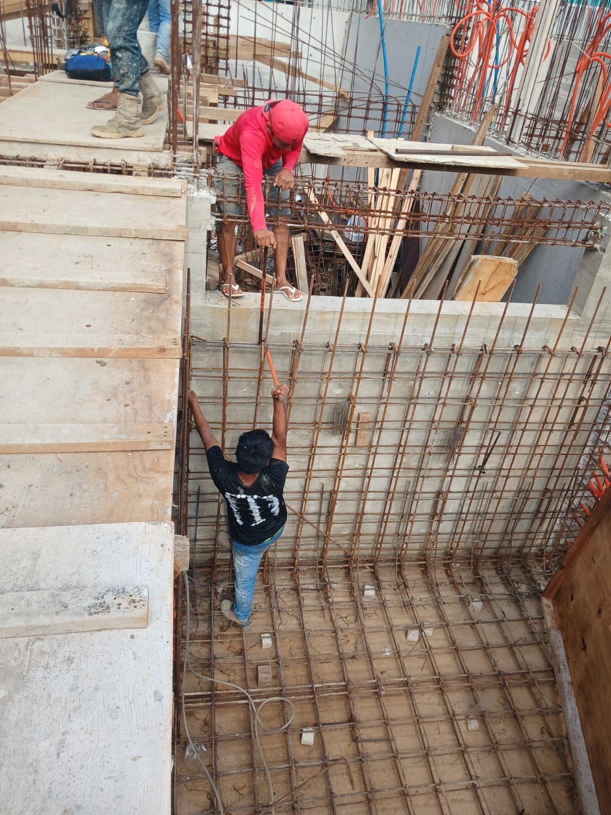 Obreros de la construcción en andamios, ensamblando una estructura de varillas de refuerzo. Un trabajador con camisa rosa, otro con camisa negra.