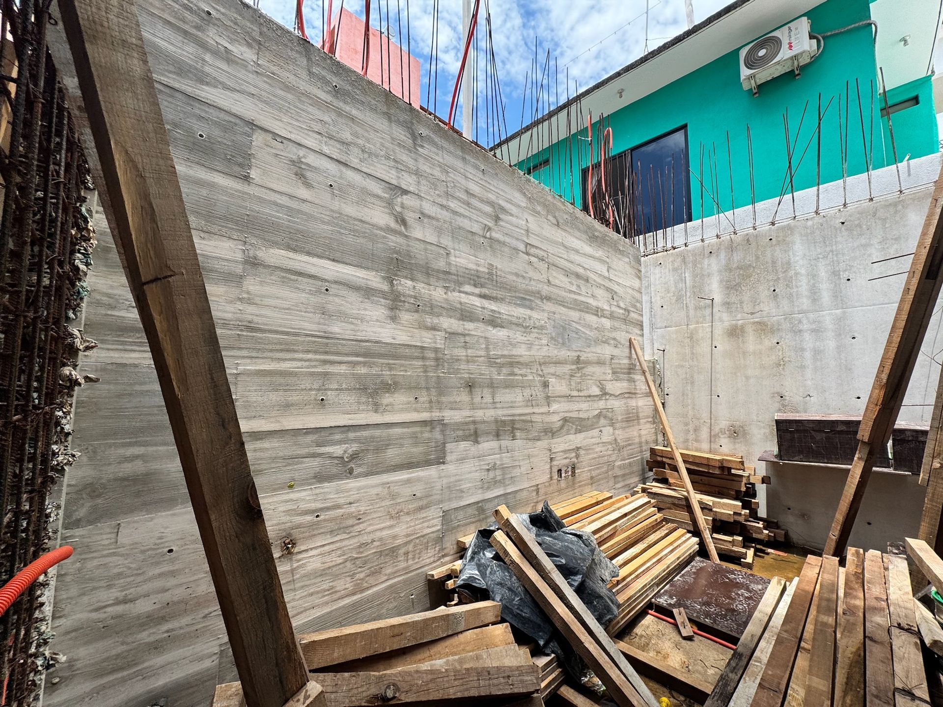 Muro de hormigón en construcción con soportes de madera y materiales de construcción.