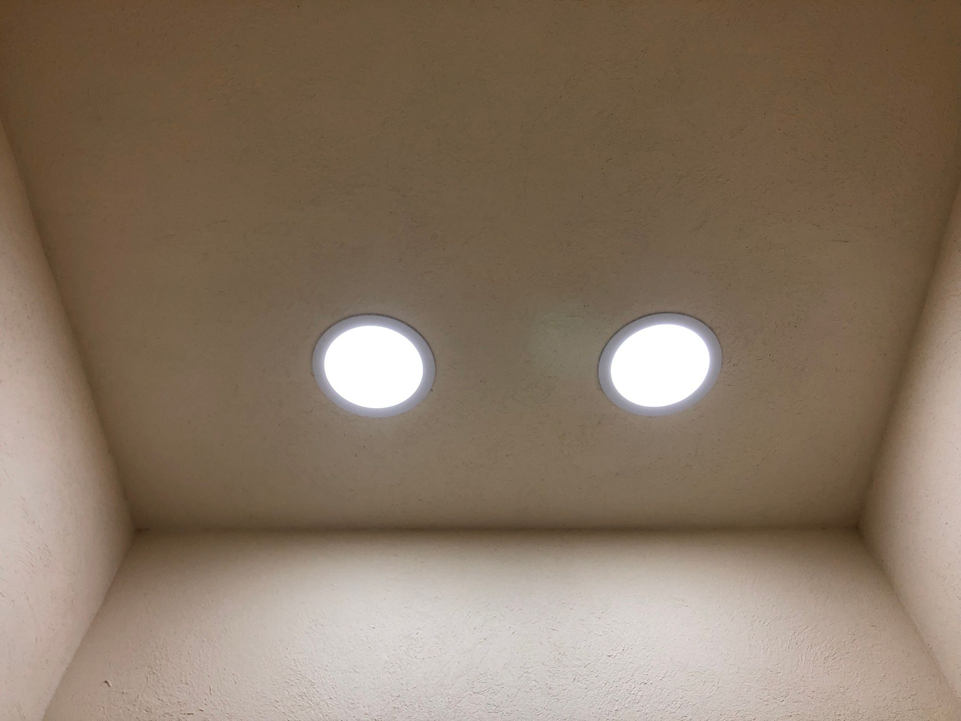 Dos lámparas de techo circulares y brillantes en una alcoba cuadrada de color beige.