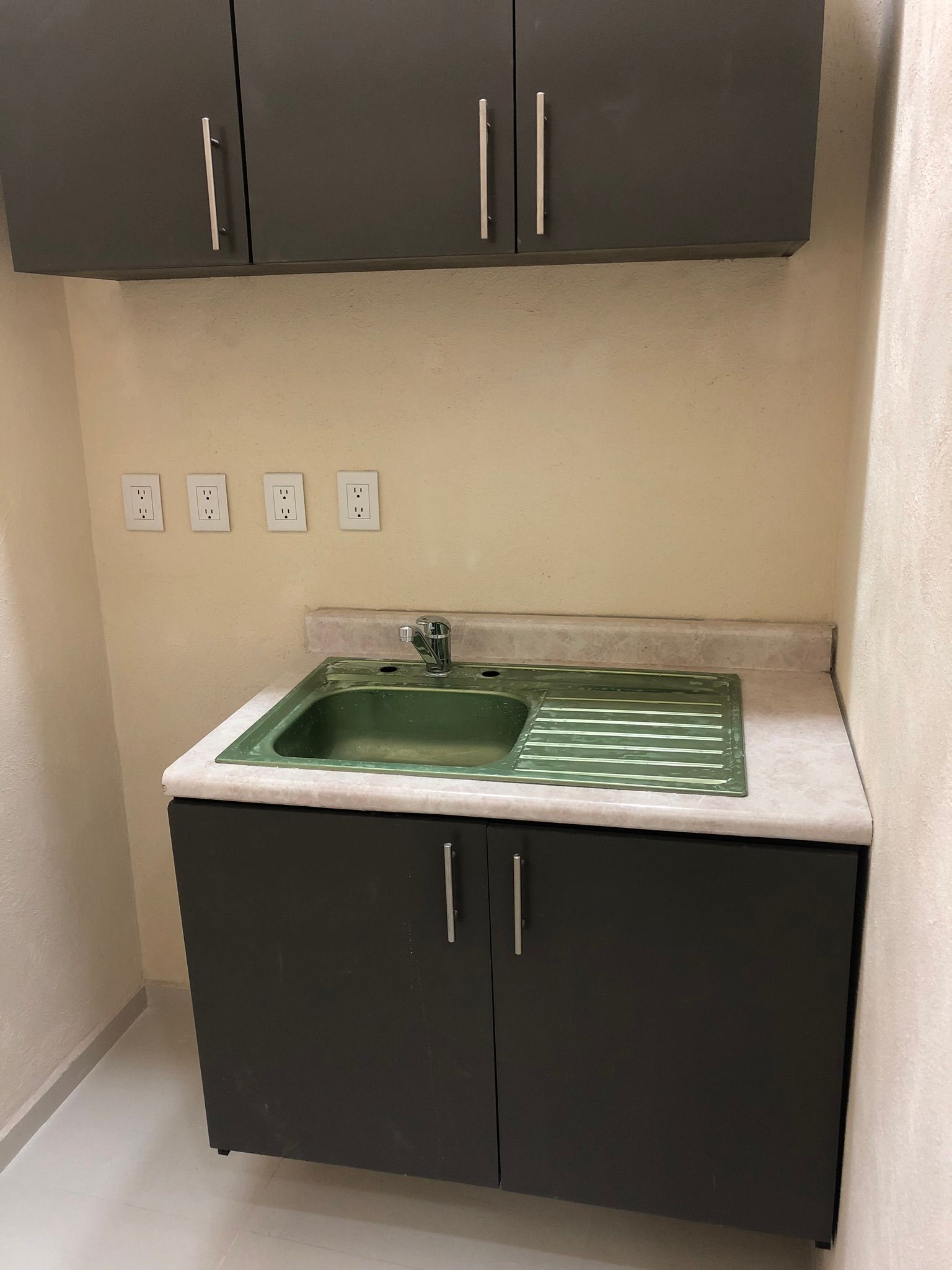 Gabinetes de color gris oscuro con un lavabo verde y una encimera blanca contra una pared beige.