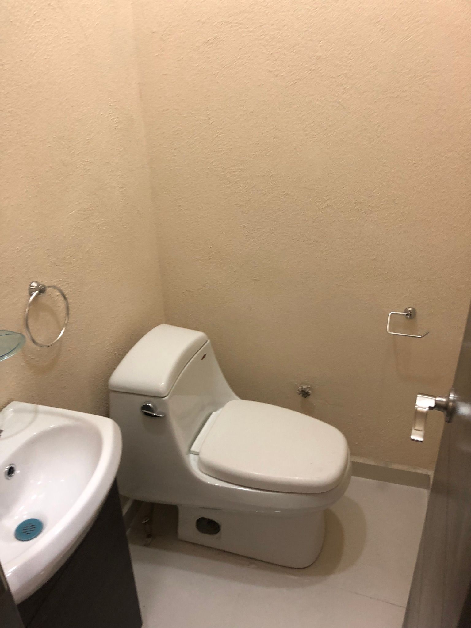 Un baño pequeño con inodoro y lavabo blancos, paredes de color marrón claro y una puerta parcialmente visible.