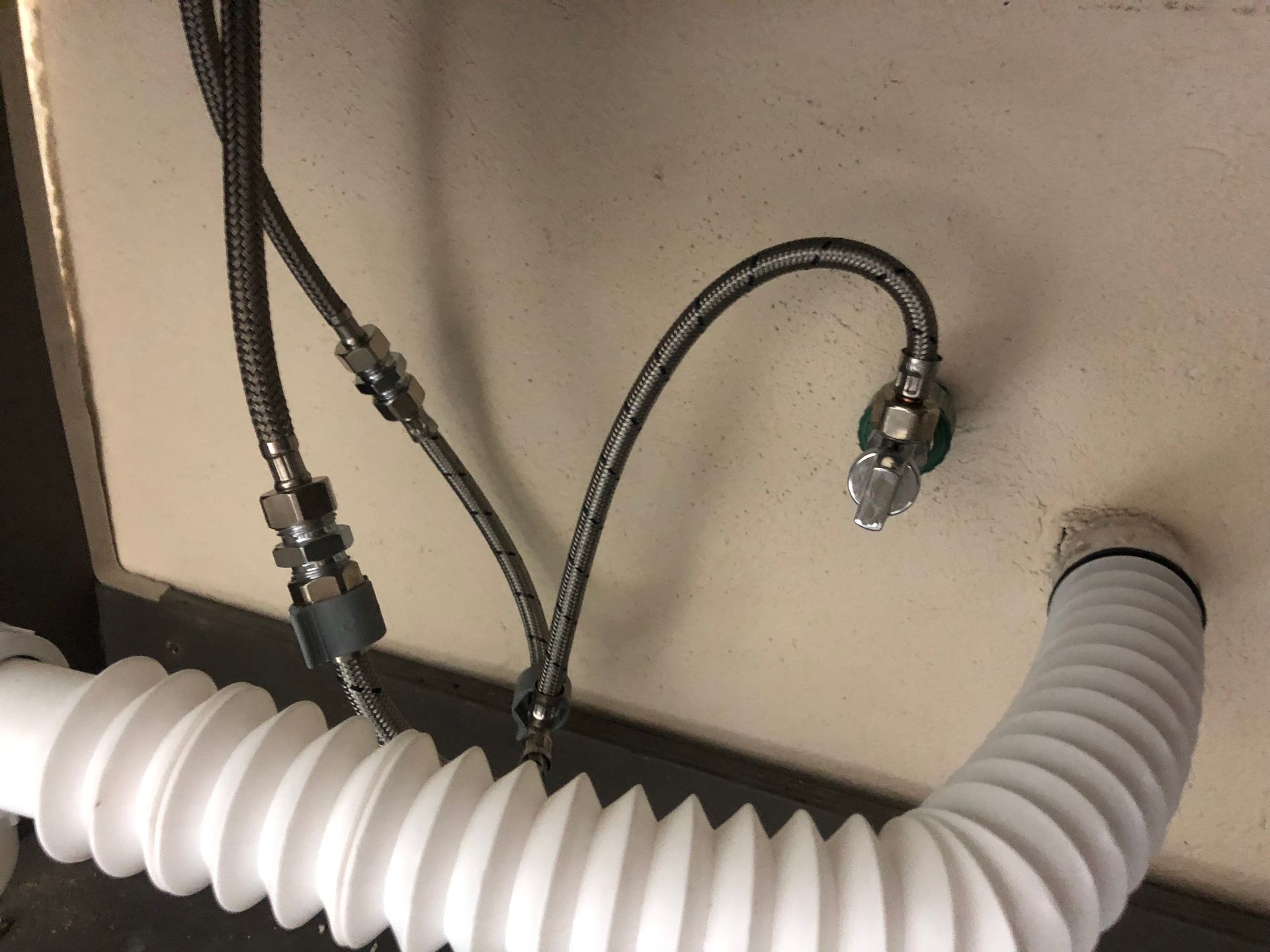 Mangueras de acero inoxidable conectadas a la pared y al tubo de desagüe debajo de un fregadero.