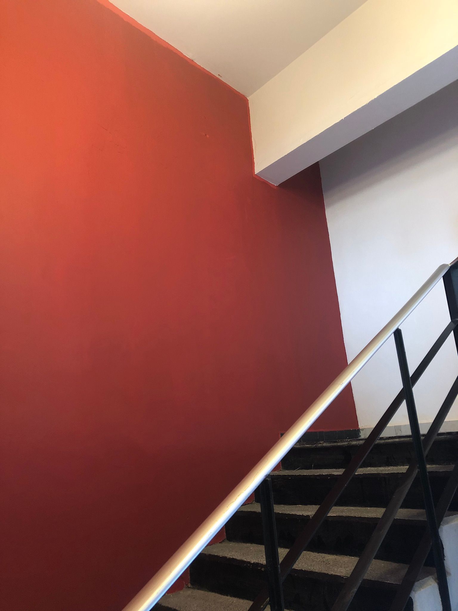 Pared roja junto a la escalera con barandilla negra. Techo y pasamanos blancos.