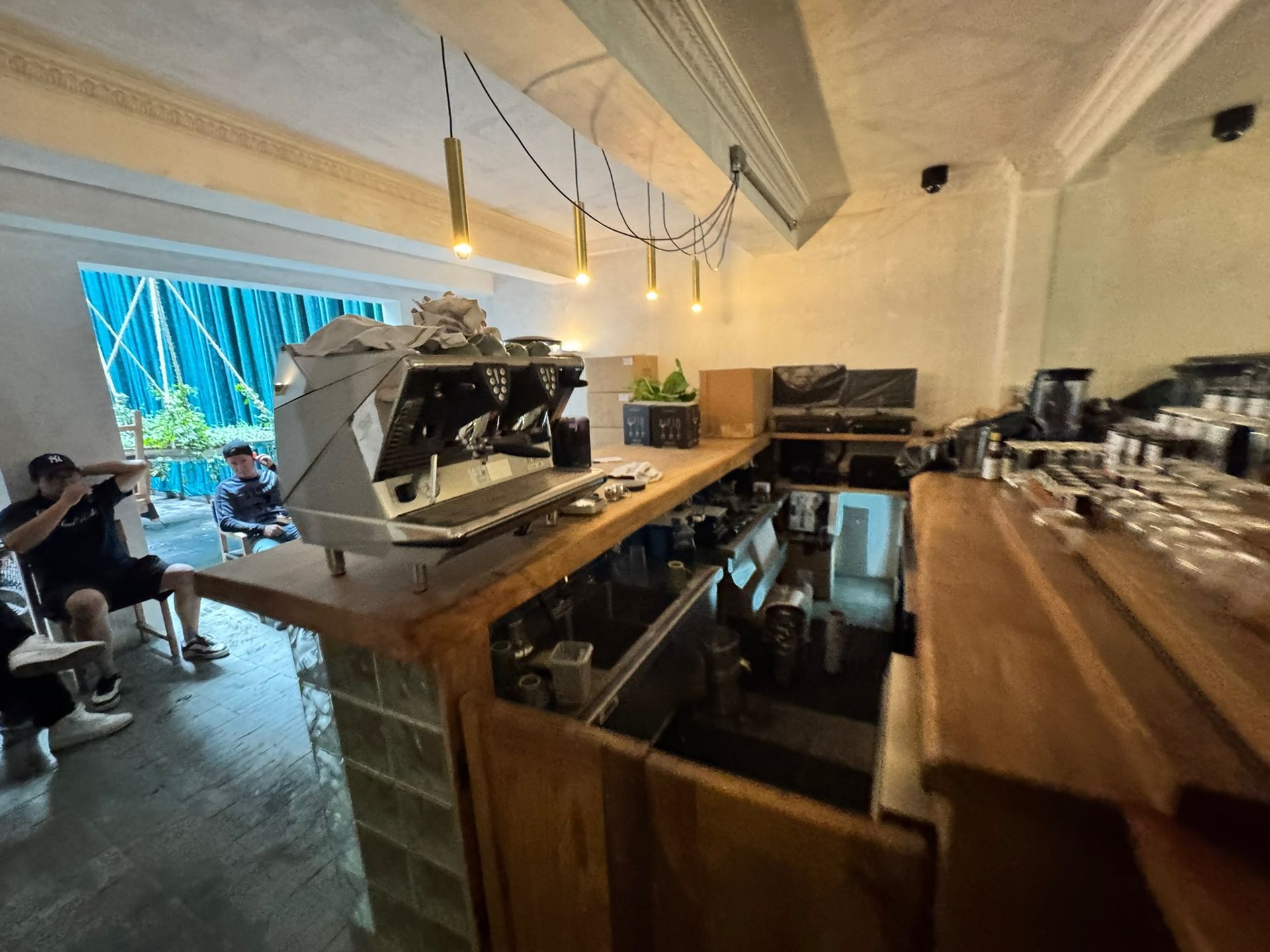 Bar de cafetería con gran máquina de café expreso y baristas; mostrador de madera, iluminación brillante.