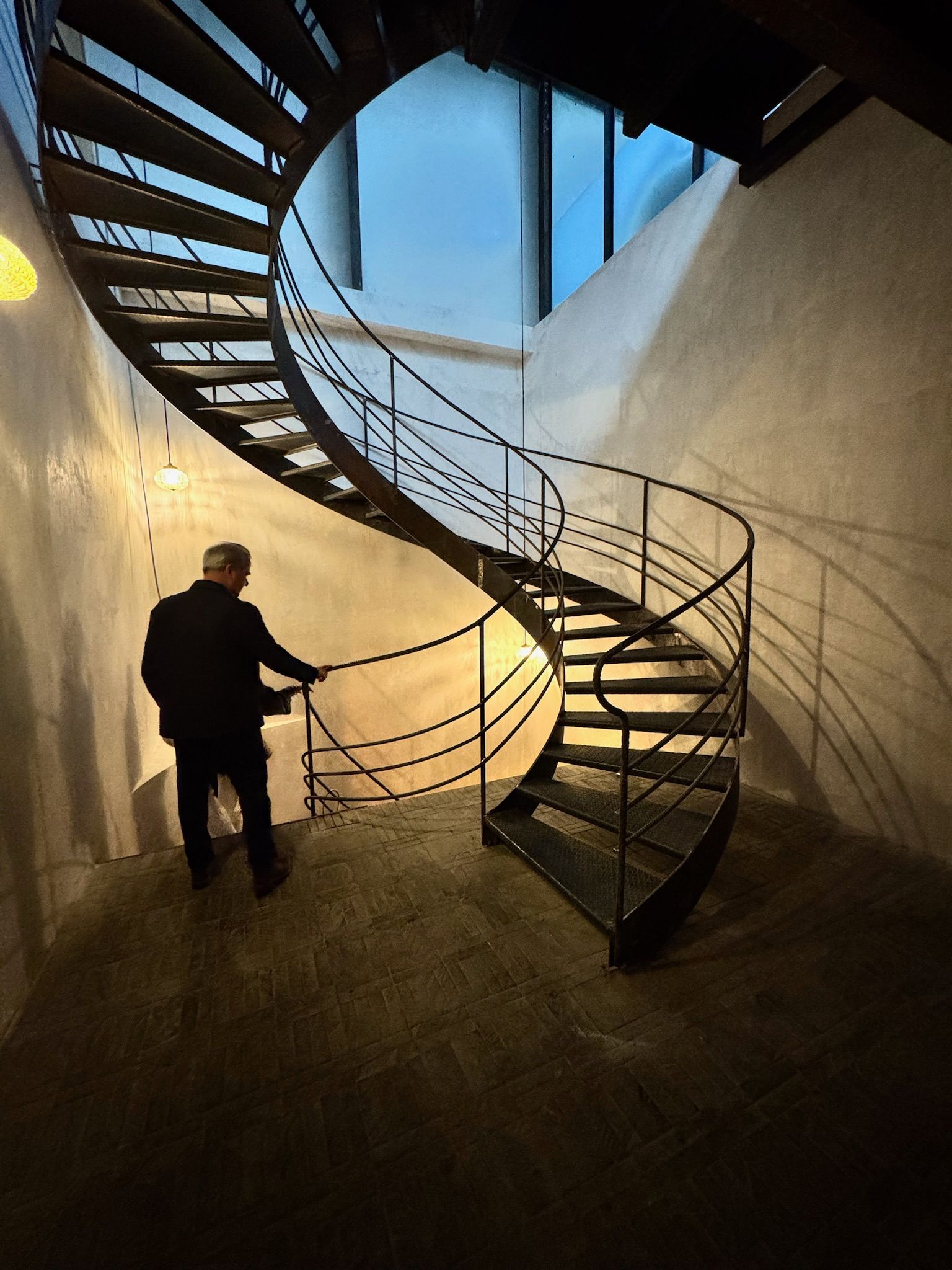 Un hombre está de pie junto a una escalera de caracol. La escalera es de metal y las paredes son de color claro.