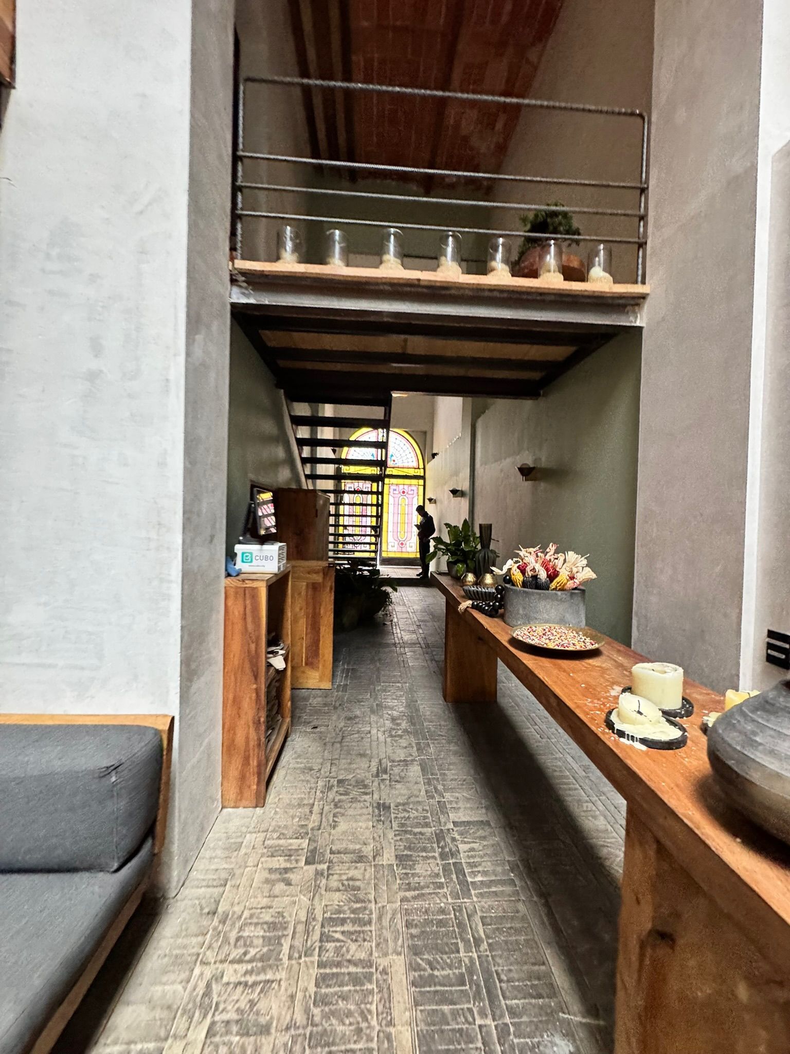 Pasillo con muebles de madera, altillo y suelo de ladrillo; persona al final cerca de una puerta amarilla.