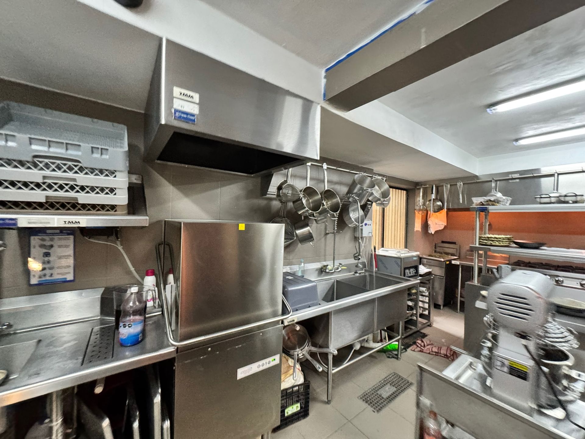 Cocina comercial, electrodomésticos de acero inoxidable, ollas colgadas, área de preparación de alimentos, ventilación superior, fregaderos, equipo.