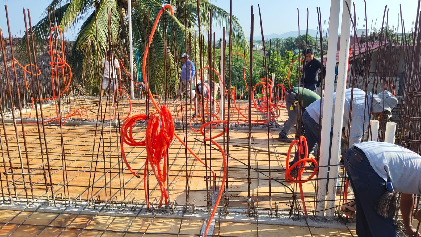 Obreros de la construcción instalando cableado eléctrico naranja en una estructura de hormigón en un tejado.