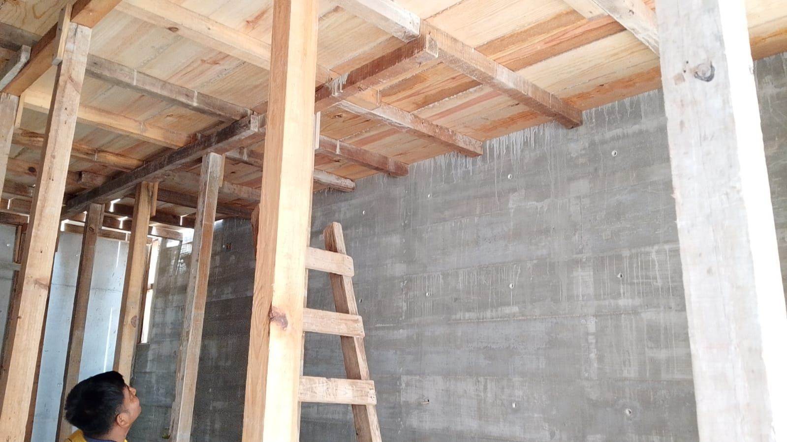 Estructura de madera de un edificio en construcción con una escalera y una persona mirando hacia el techo.