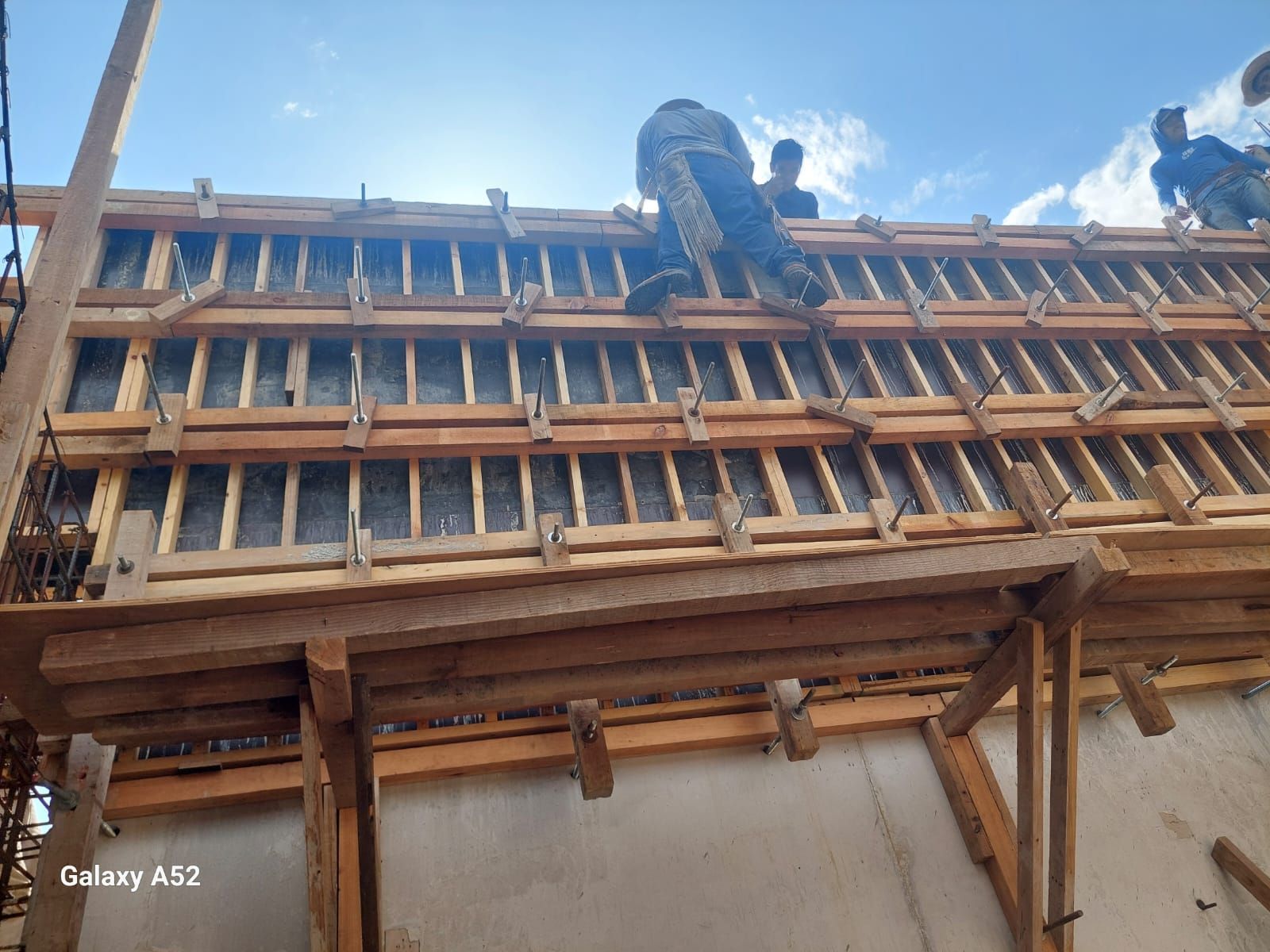 Obreros de la construcción en andamios, construyendo un encofrado de madera contra un cielo azul.