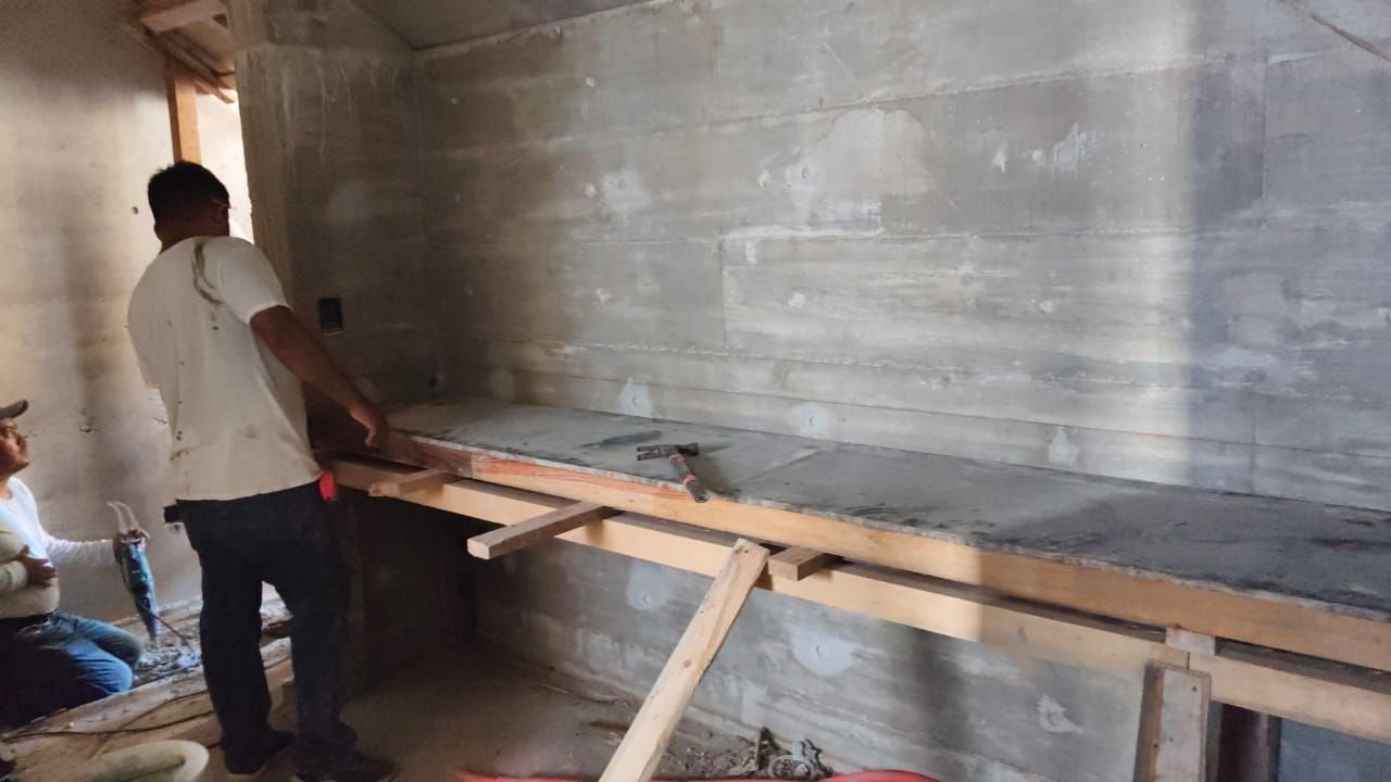 Dos hombres trabajando en una encimera de hormigón en una habitación en construcción.