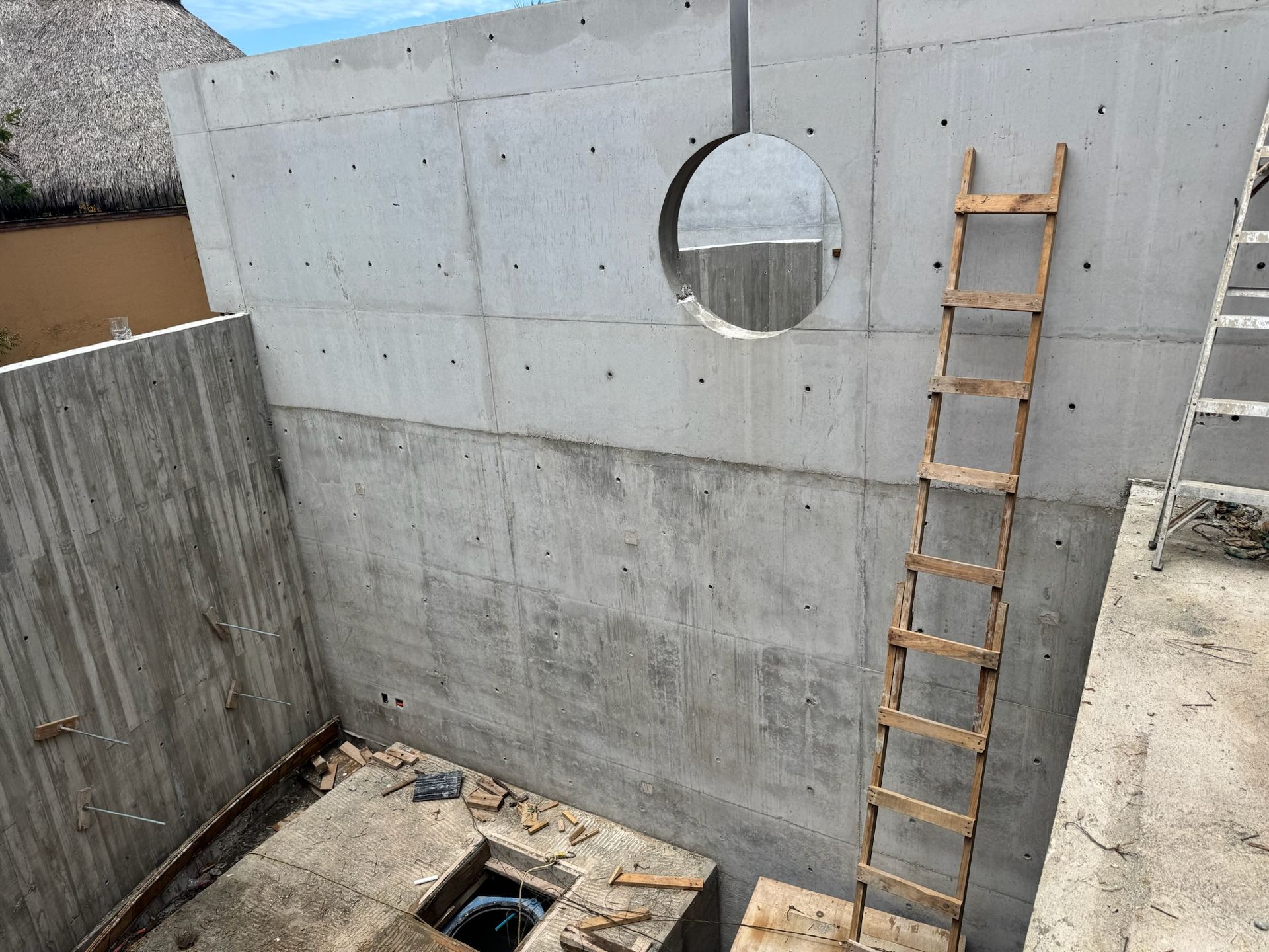 Estructura de hormigón en construcción con abertura circular, escalera de madera y planta abierta.