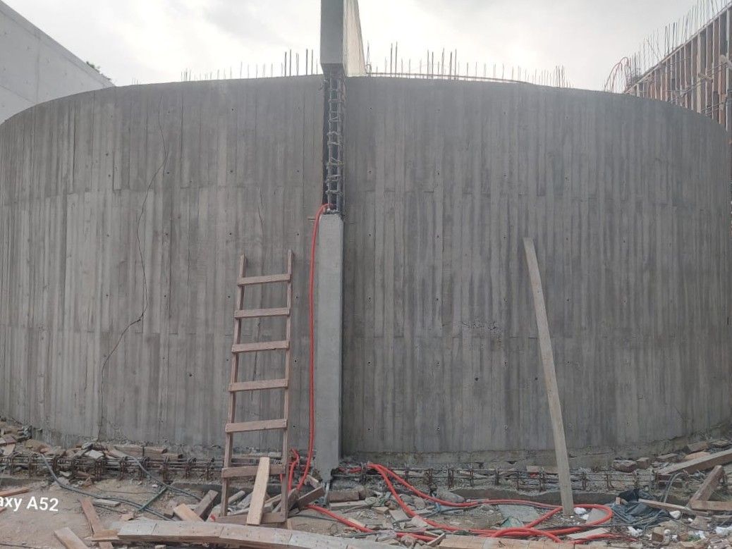 Sitio de construcción con un alto muro de hormigón, escalera y barras de refuerzo expuestas.