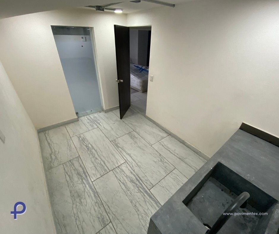 Habitación vacía con piso de baldosas, dos puertas y un mostrador gris con lavabo.