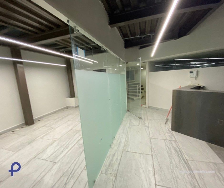 Espacio de oficina vacío con paredes de vidrio y piso de baldosas.