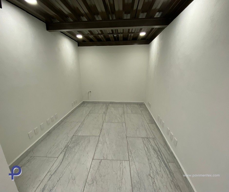 Habitación vacía con suelo de baldosas grises, paredes blancas y techo con paneles de madera.