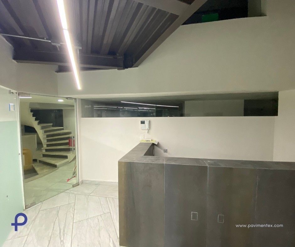 Interior de oficina moderno con mostrador de recepción, escaleras y puerta de vidrio.
