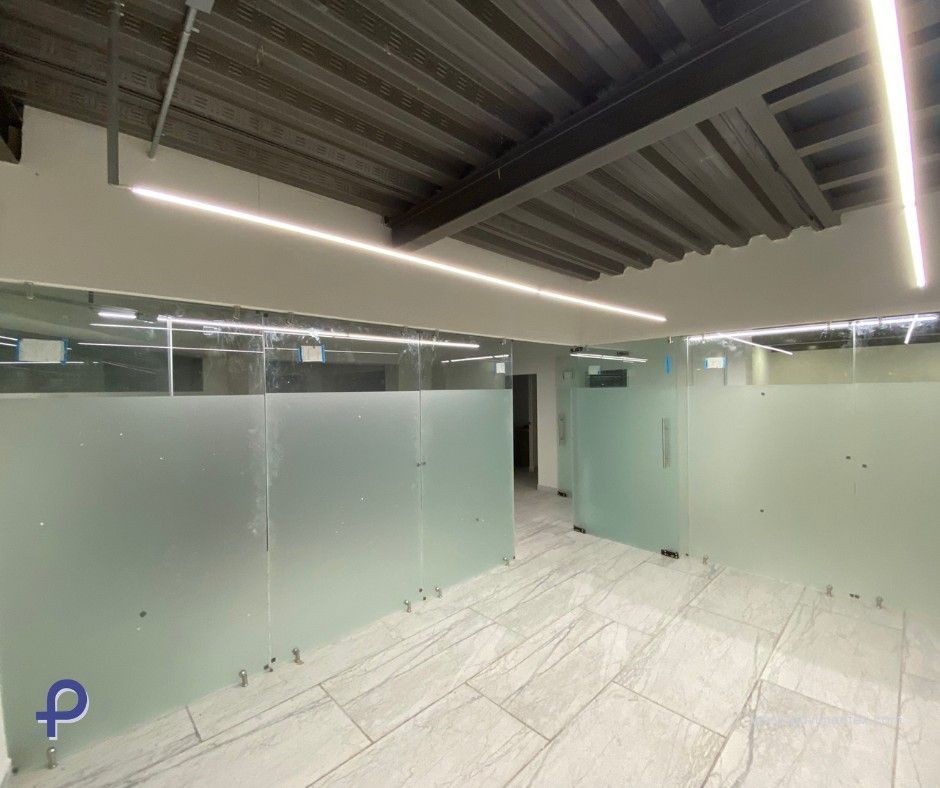 Espacio de oficina vacío con paredes de vidrio esmerilado e iluminación superior brillante.