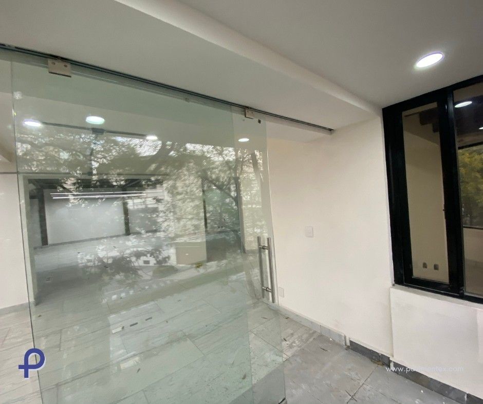 Local comercial vacío con escaparate de cristal y gran ventanal; suelo de baldosas grises y paredes neutrales.