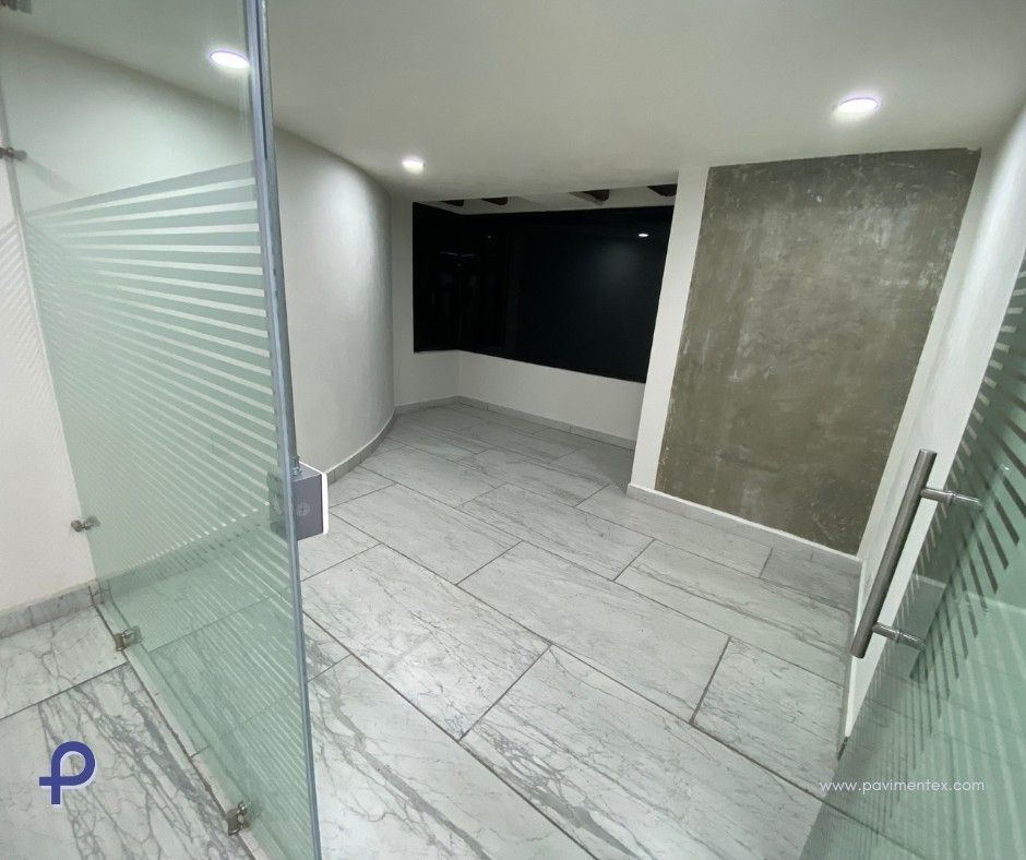 Oficina vacía con piso de baldosas grises y puerta de vidrio esmerilado.