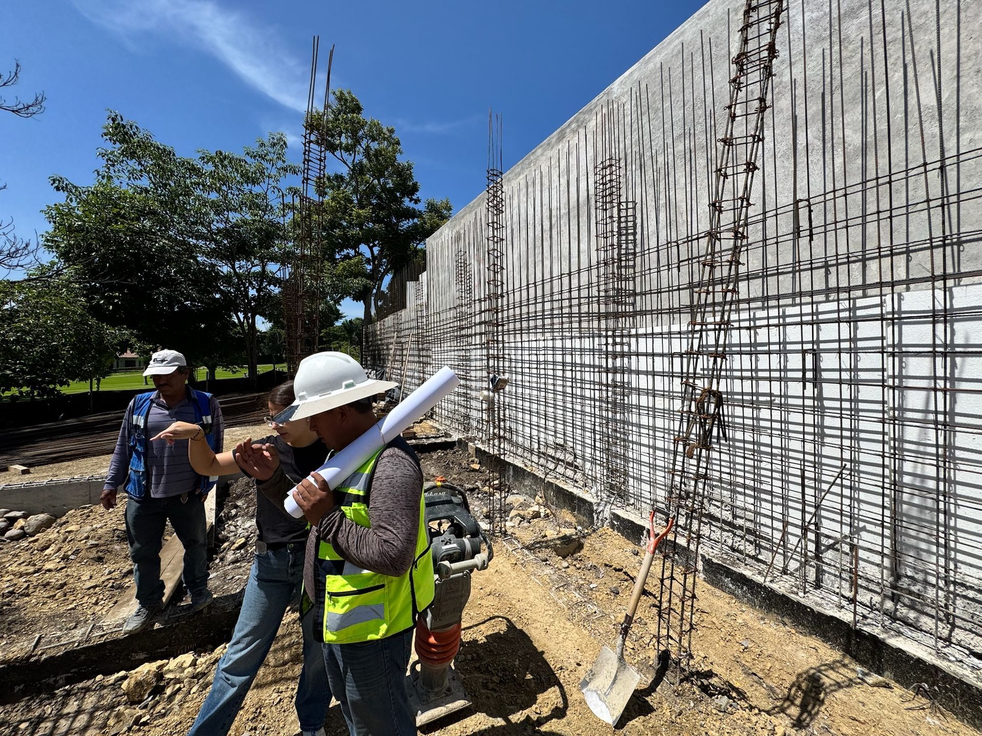 Obreros de la construcción inspeccionan una pared de varillas de refuerzo en un sitio en un día soleado.