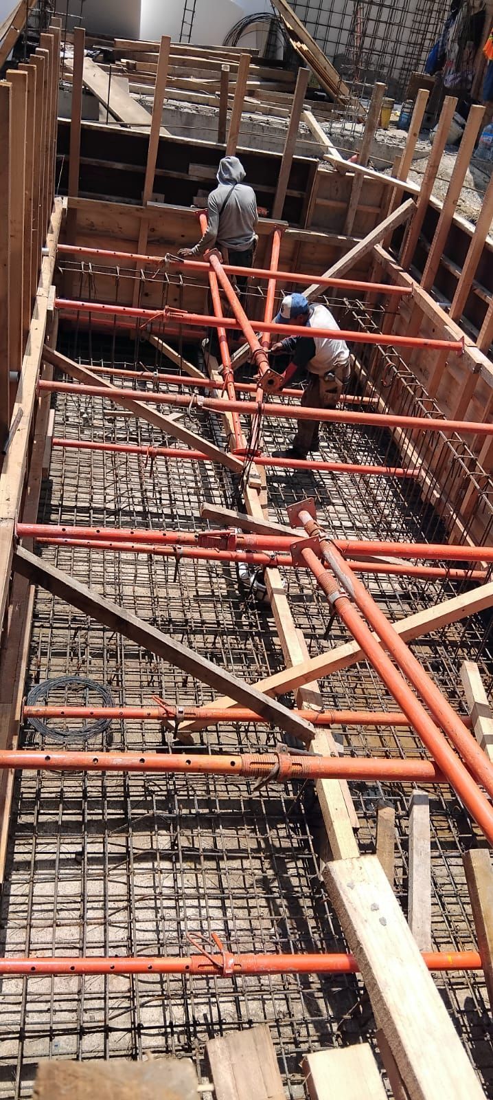 Obreros de la construcción trabajando en una estructura de hormigón, utilizando andamios metálicos y marcos de madera.