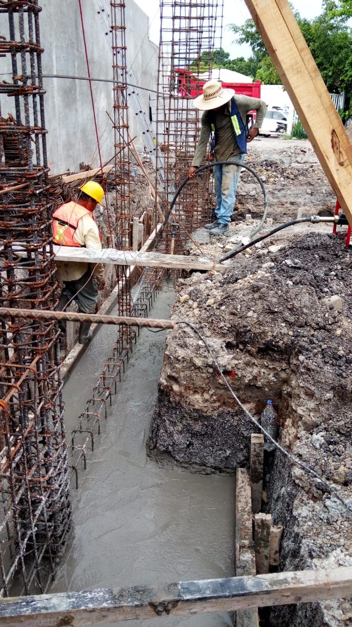 Obreros de la construcción vierten hormigón, con cascos y chalecos. El hormigón se vierte en un armazón.