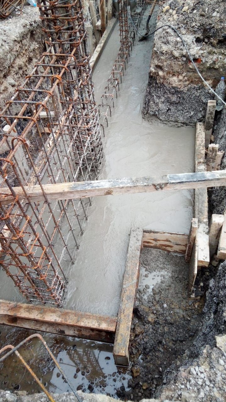 Hormigón vertido en encofrado de madera, con jaula de armadura en zanja.