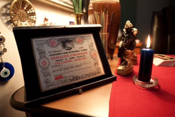 Un certificato incorniciato con testo in rumeno è appoggiato su un tavolo di legno accanto a una candela blu accesa e a una piccola statua.