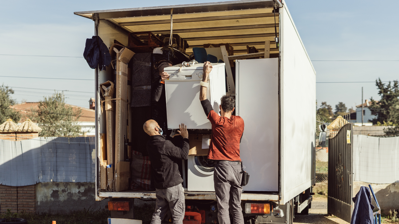 Two people loading a white appliance into a truck, outdoors.