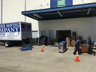 Moving truck loading furniture outside a building. Workers carrying items.