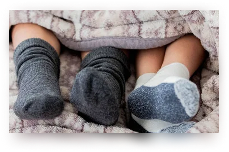 Four feet wearing gray socks tucked under a blanket.
