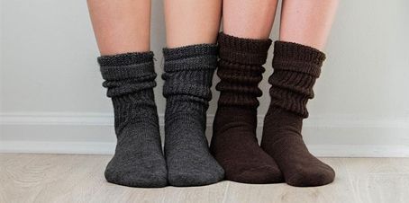 Four pairs of legs in gray and brown knit socks, standing on wood flooring against a white wall.