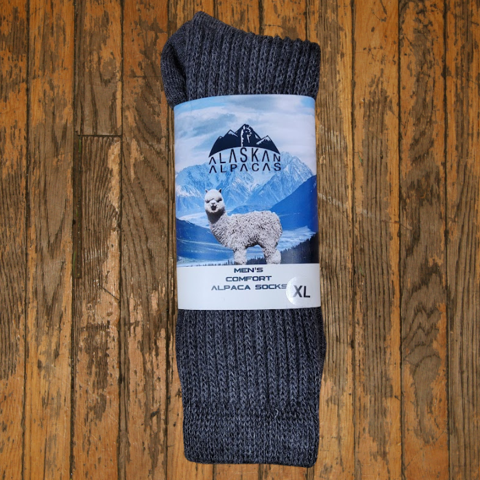 Gray alpaca socks with a label showing an alpaca and mountains, on a wooden surface.