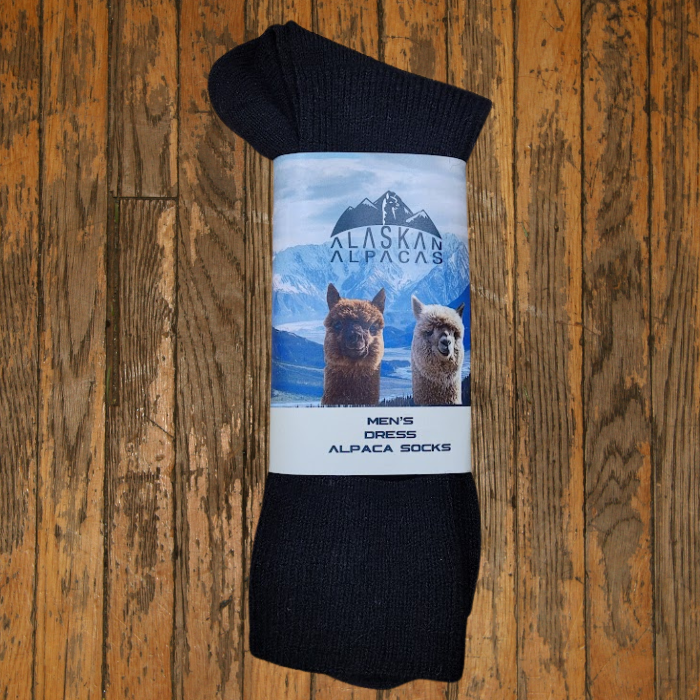 Black socks with a label featuring alpacas and mountains, on wood.