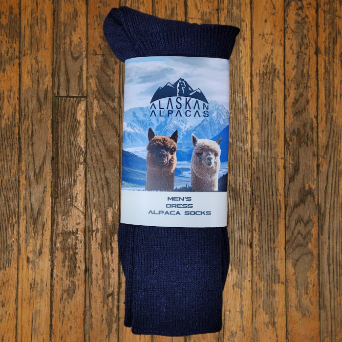 Dark blue alpaca socks with a label featuring two alpaca heads and snowy mountains on a wood background.