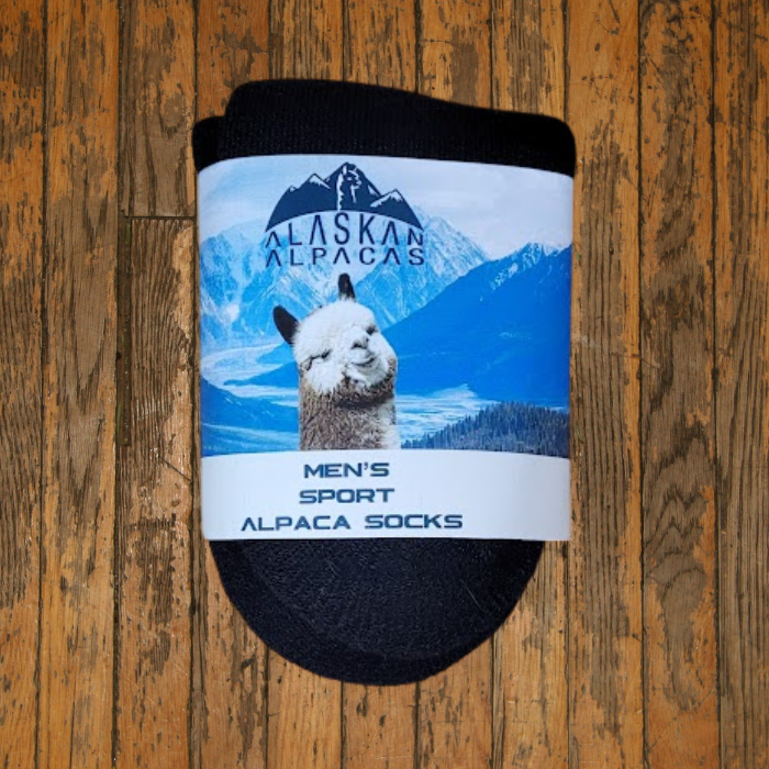 Black alpaca socks with a label showing an alpaca in a snowy mountain scene on a wood surface.