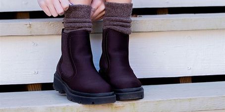 Person adjusting brown socks over dark brown boots on wooden steps.