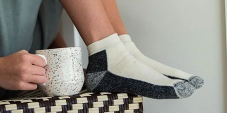 Person holding a speckled mug, feet up wearing cream-colored socks with dark gray accents.
