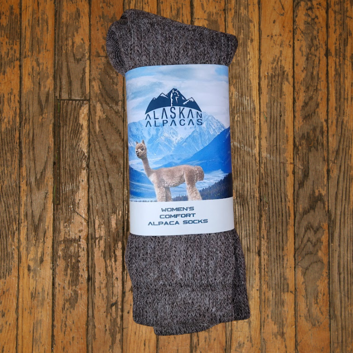 Pair of gray alpaca socks with a label featuring an alpaca and mountains, on wooden surface.