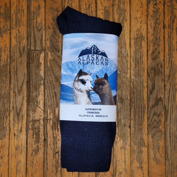 Dark gray socks wrapped with a label that features two alpacas in front of a mountain scene, on a wood surface.