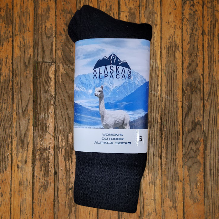 Black alpaca socks with a label showing an alpaca and mountains on a wooden surface.