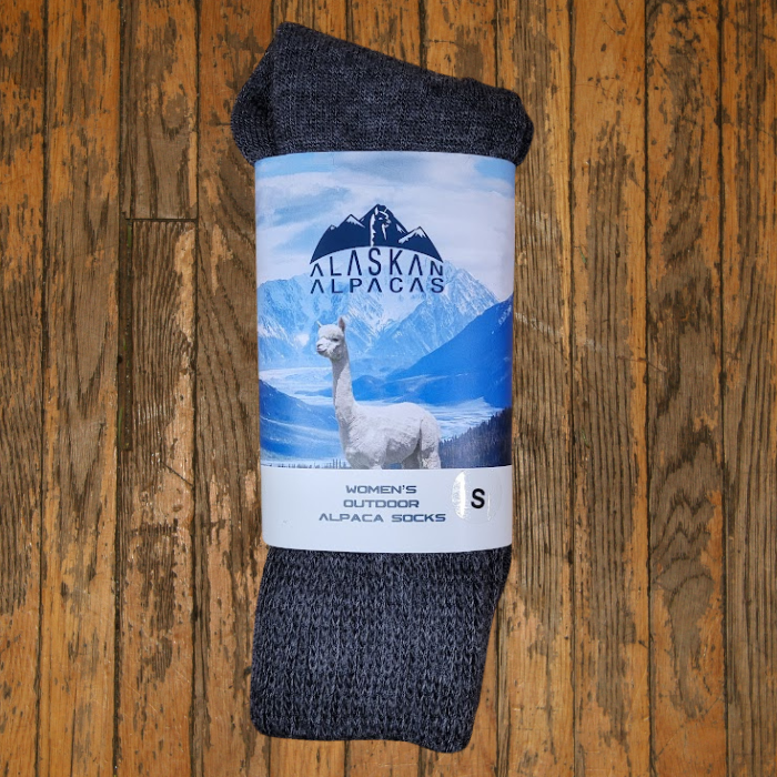 Dark gray Alaska Alpaca socks in packaging, on a wooden surface.