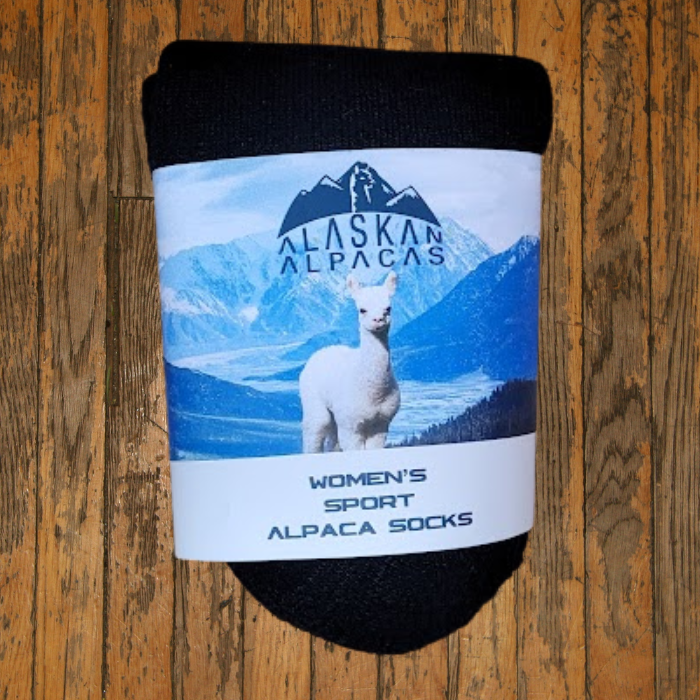 Black rolled socks with label featuring an alpaca and snowy mountains on a wooden surface.
