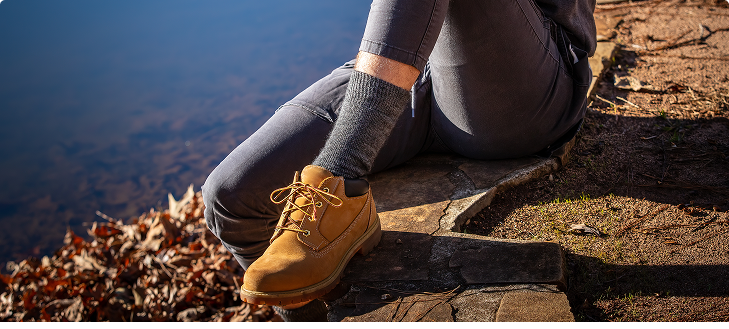 Person sitting on a stone ledge, wearing tan boots. A body of water is in the background.