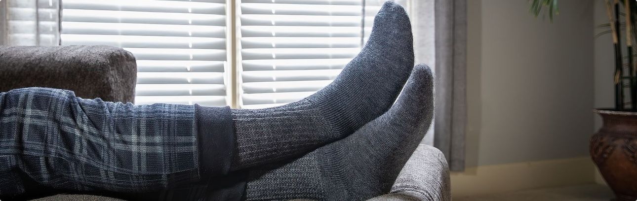 Person relaxing on a couch, feet up, wearing gray knit socks, near a window.