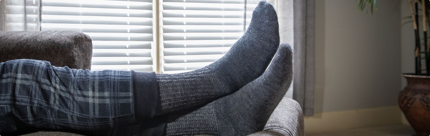 Person relaxing on a couch, feet up, wearing gray knit socks, near a window.