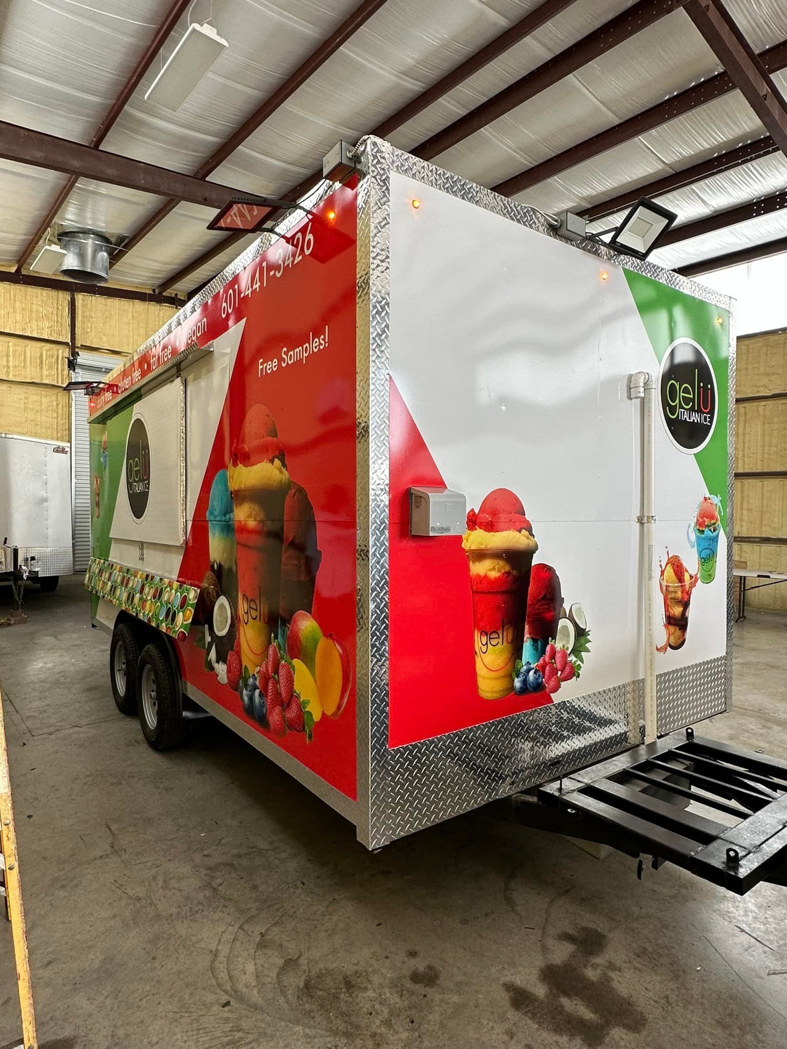 A technician wearing gloves uses a squeegee to apply an orange vinyl wrap to the side of a white van in a workshop.